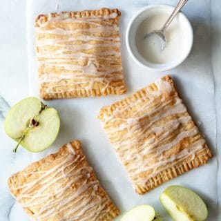 a close up of three apple turnovers with a glaze drizzled on top, next to slices of green apple