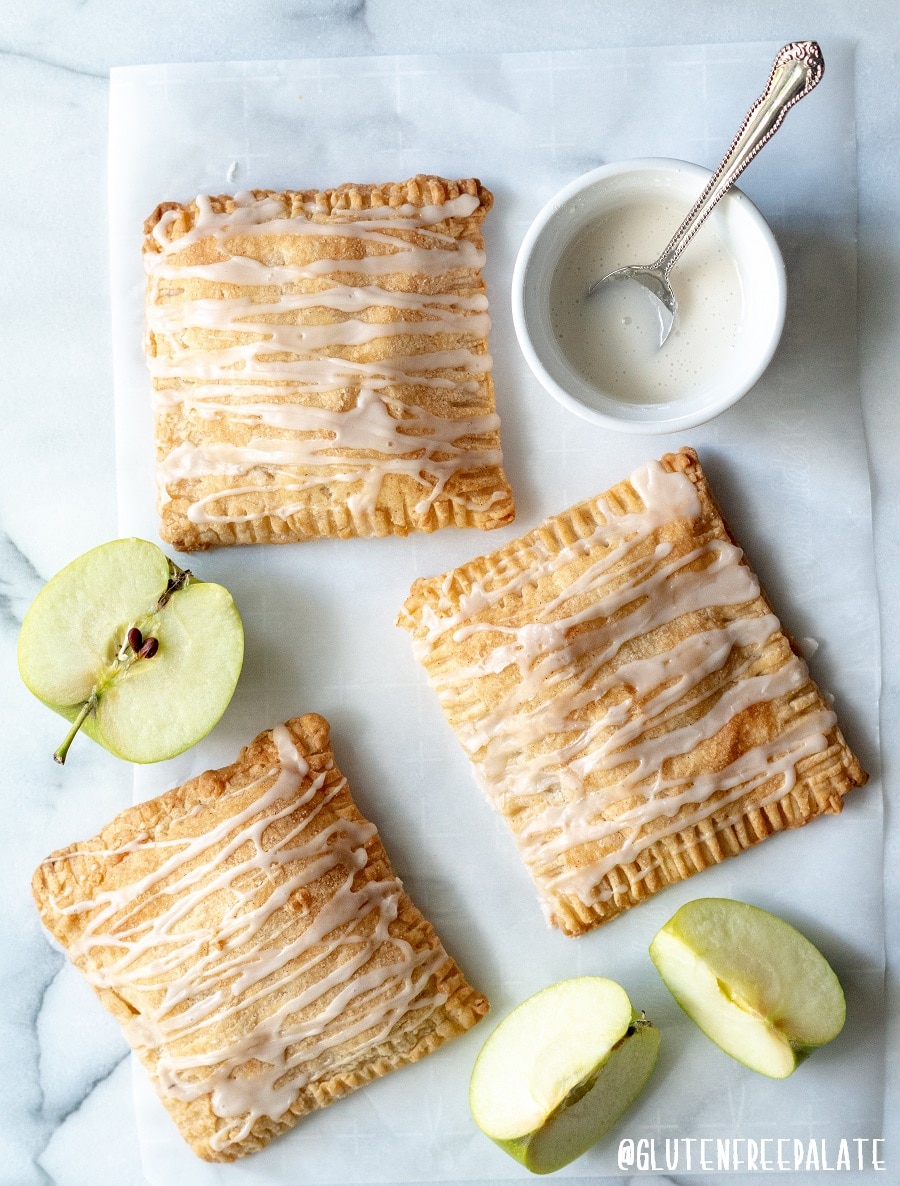 a close up of three apple turnovers with a glaze drizzled on top, next to slices of green apple