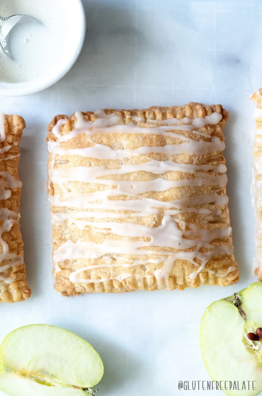 a close up of a apple turnover with a glaze drizzled on top, next to slices of green apple
