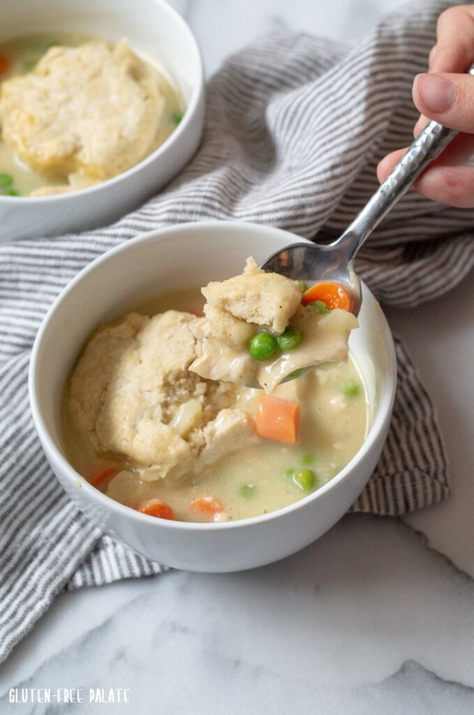 A close up of chicken filling and a biscuit in a white bowl with a spoon showing a bite