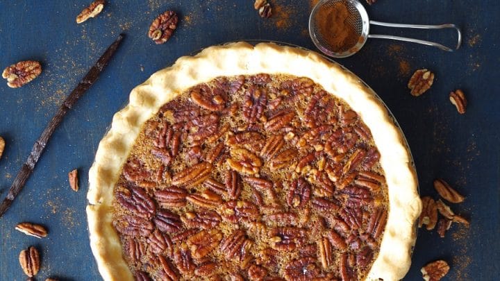 a paleo pecan pie in a pie plate with scattered pecans around it