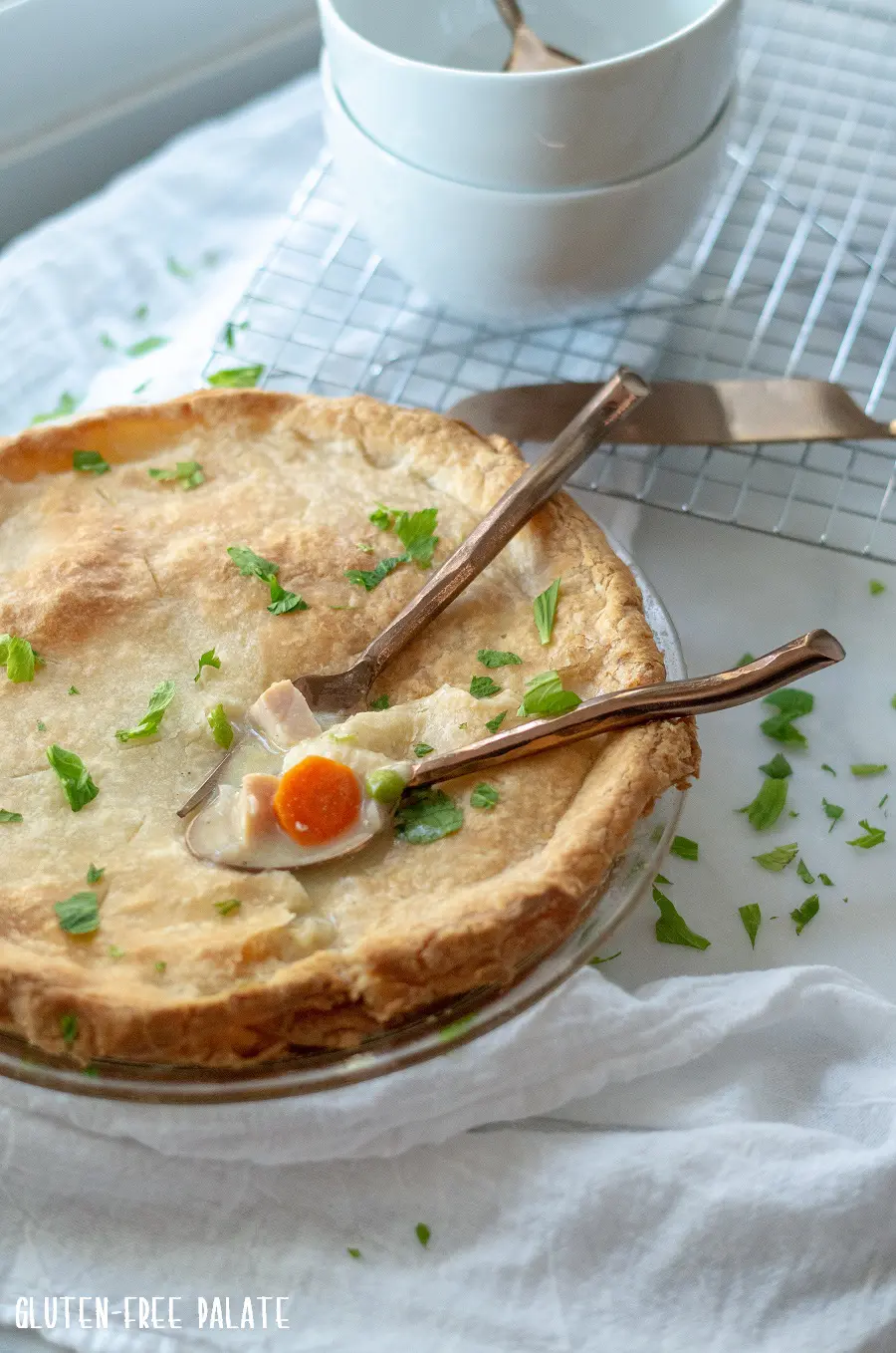 a side view of gluten free turkey pot in in a glass pie pan with two spoons dipped into the pie