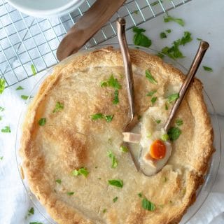 a close up of gluten free turkey pot in in a glass pie pan with two spoons dipped into the pie