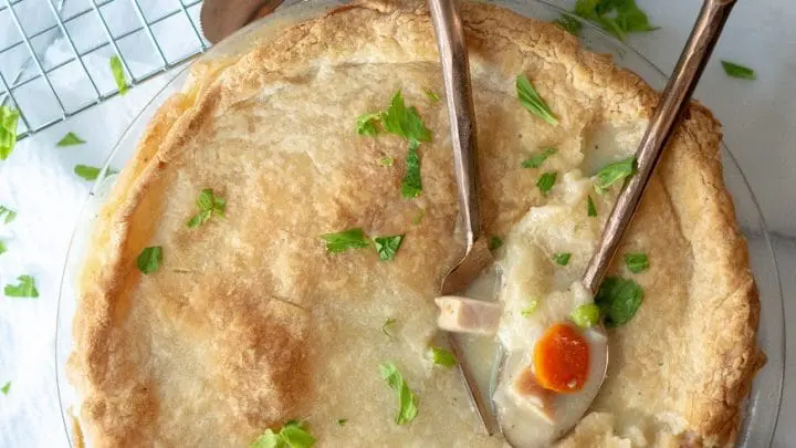 a close up of gluten free turkey pot in in a glass pie pan with two spoons dipped into the pie