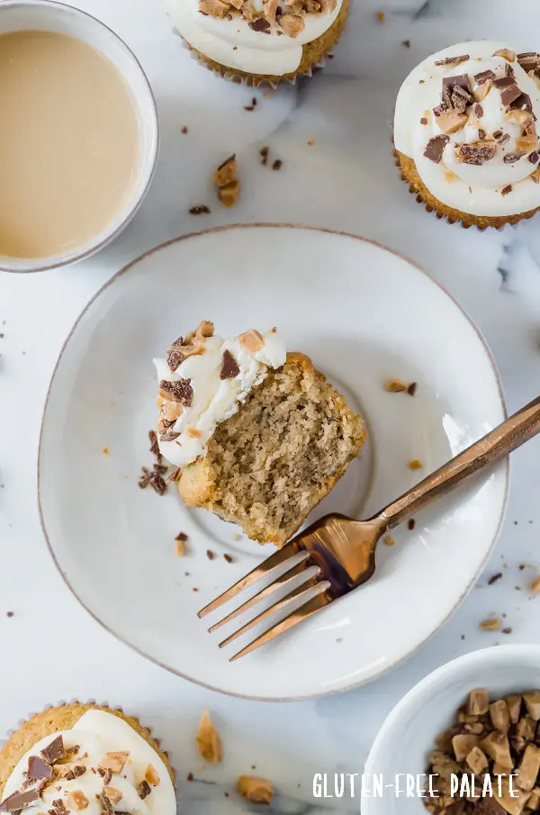 grain-free banana toffee cupcake with frosting cut in half, on a white plate with a gold fork