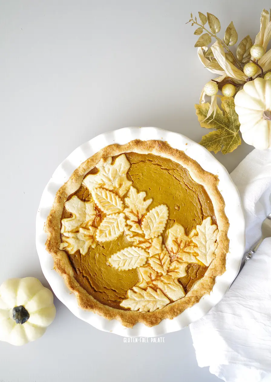 a gluten-free pumpkin pie in a white dish with the top crust shaped like leaves