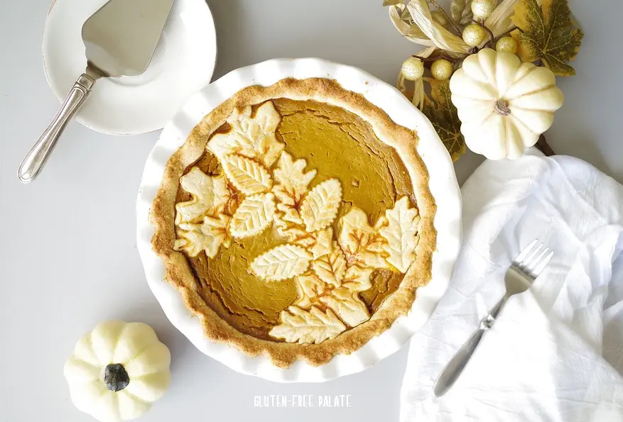 pumpkin pie in a white pie pan next to white pumpkins and a fork and serving knife