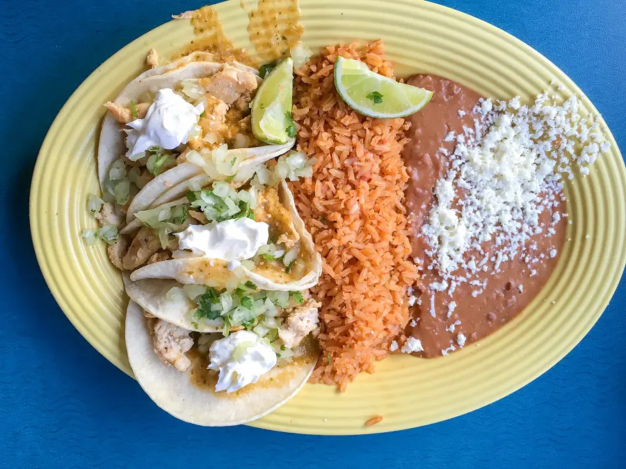 a yellow plate filled with three tacos, mexican rice, and refried beans