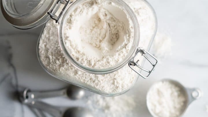 gluten-free flour in a clear jar with measuring cups and spoons next to it