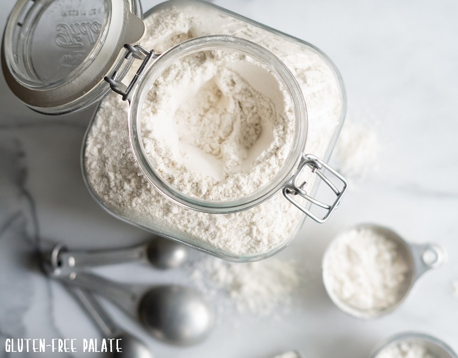 top down view of gluten-free flour in a clear jar with measuring cups and spoons next to it