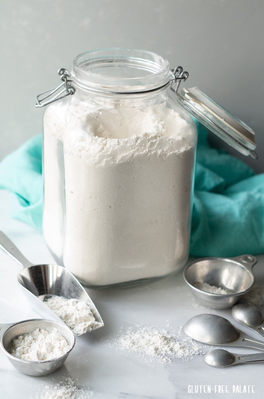 gluten-free flour in a clear jar with measuring cups and spoons next to it, a blue napkin behind it