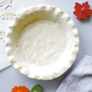 unbaked pie crust in a pan with leaf shaped cookie cutters next to it