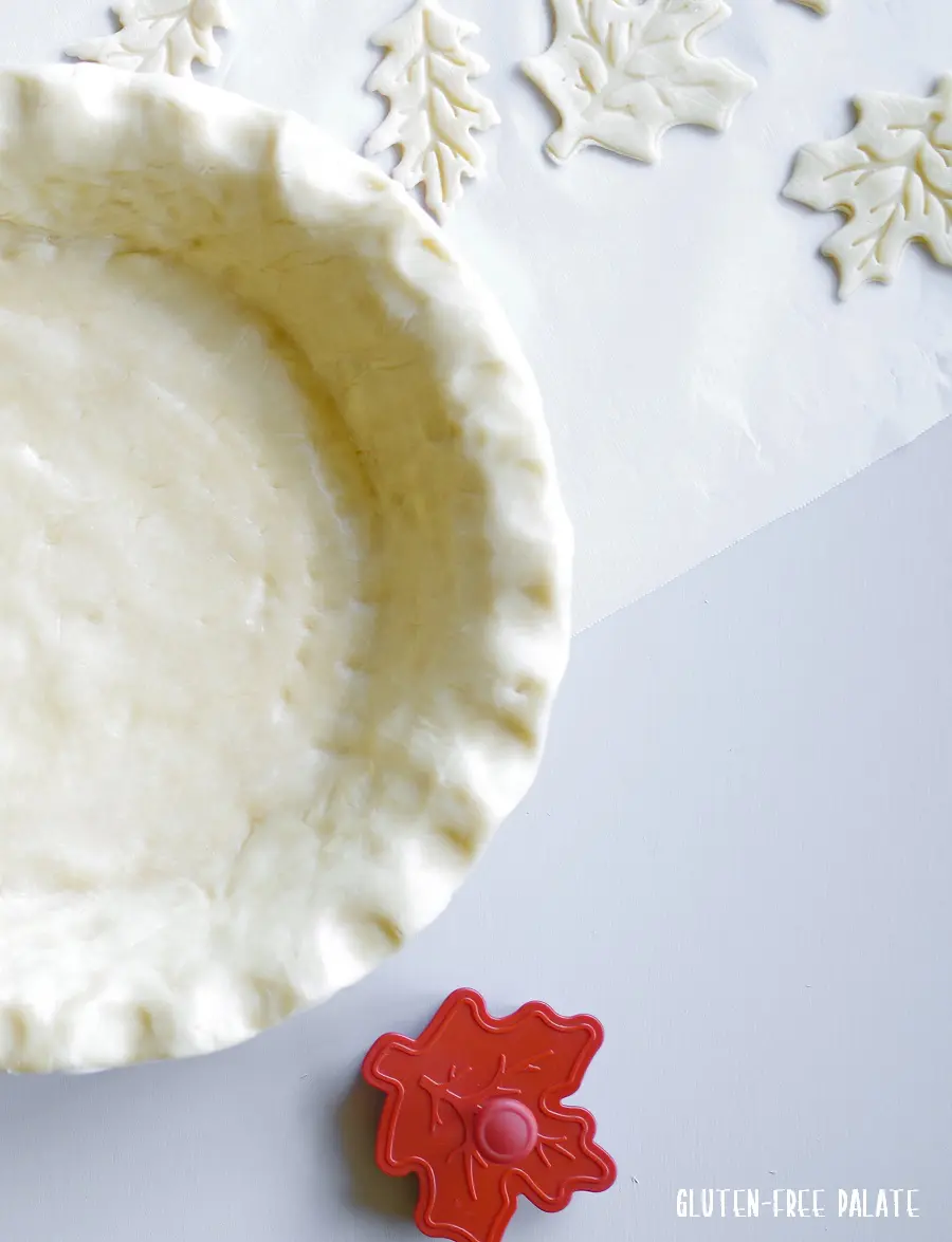 a side view of an unbaked pie crust in a pan with leaf shaped cookie cutters next to it