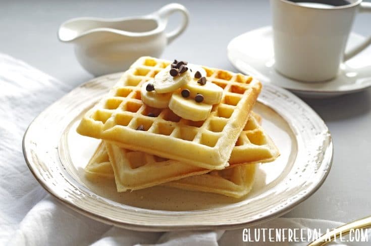 three stacked Gluten-Free Waffles topped with sliced banana and chocolate chips next to a cup of coffee