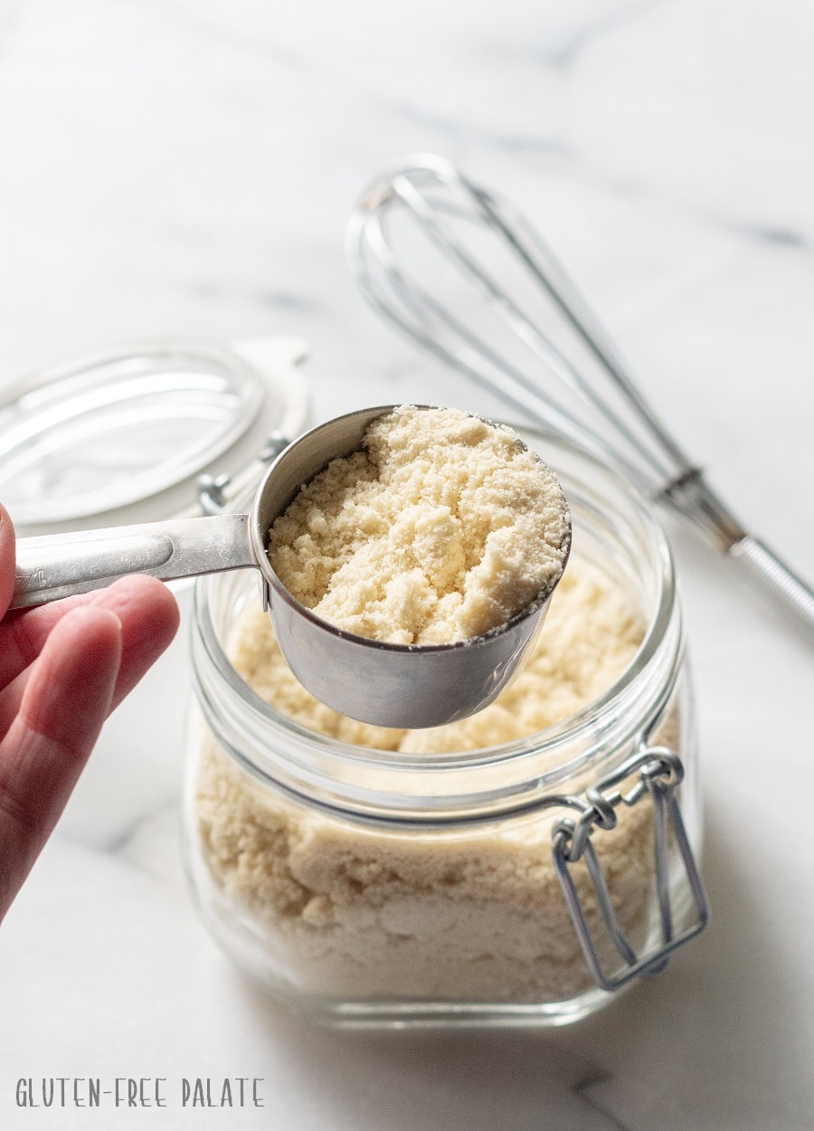 a glass jar filled with paleo pancake mix with a hand scooping out a measuring cup of mix