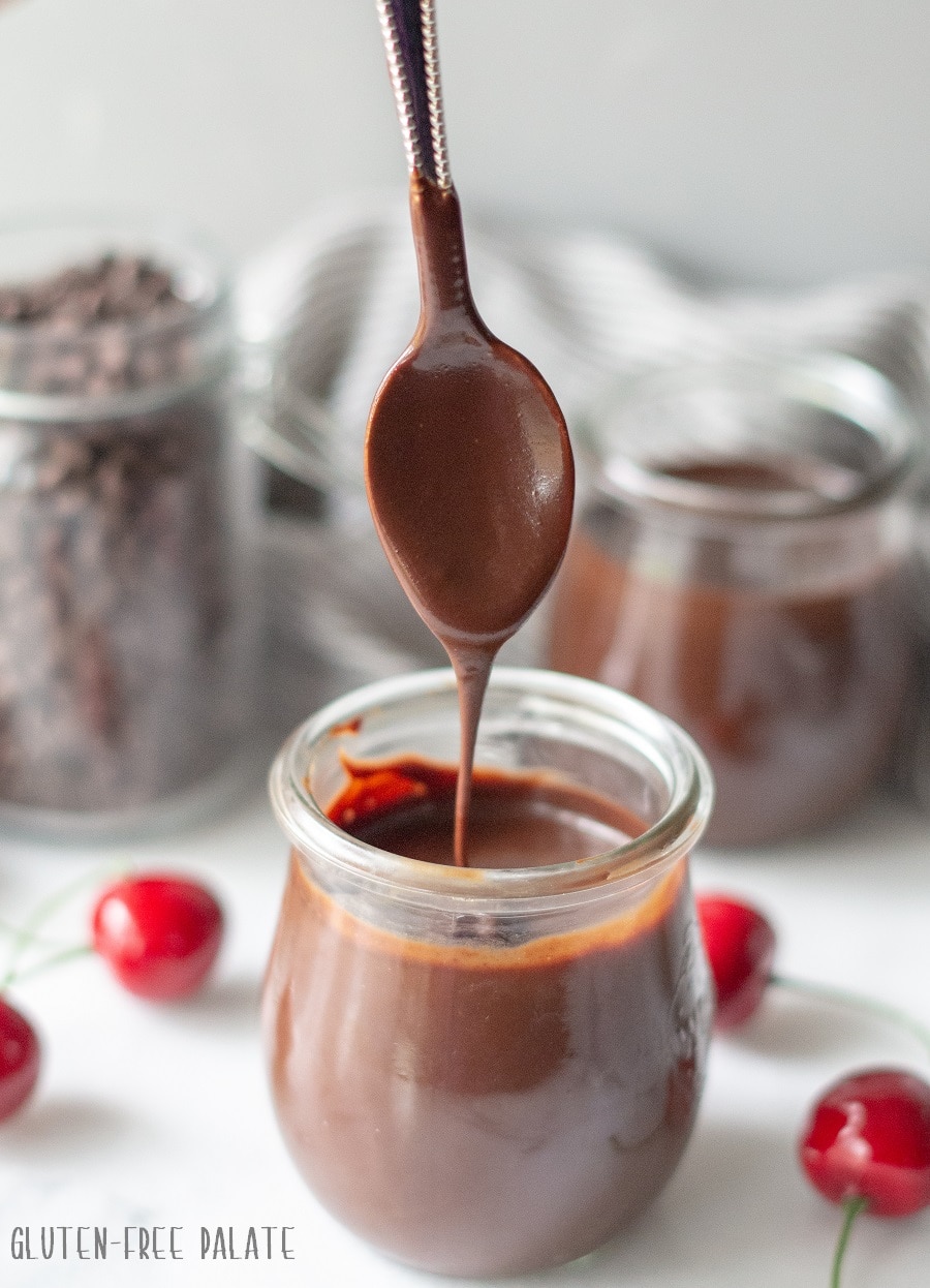 chocolate sauce in a clear jar with a spoon dipped in with cherries on the side