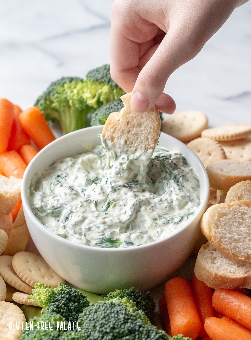 a hand dipping bread into a bowl of spinach dip