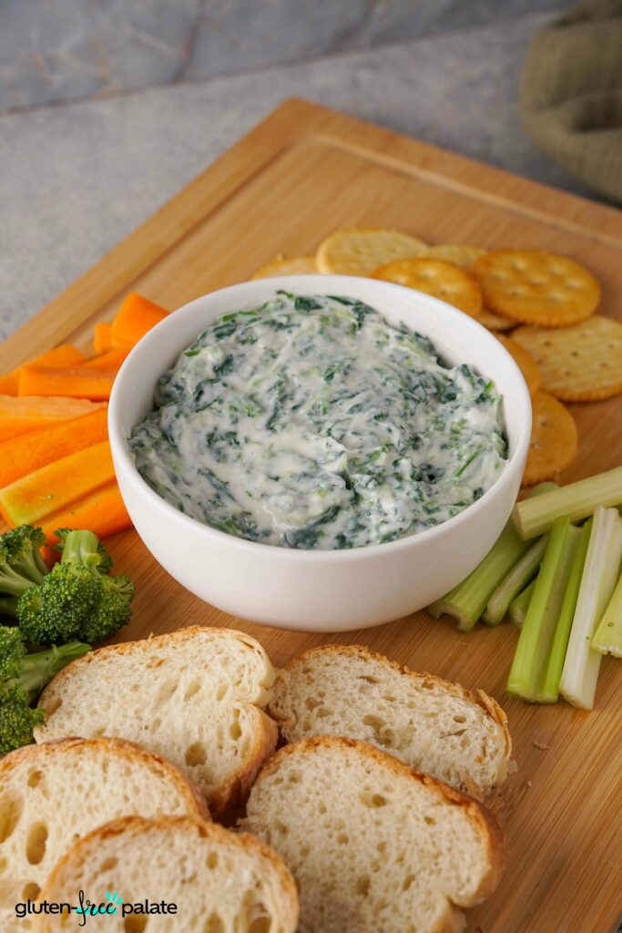 Gluten-free spinach dip on a board with veggies, bread and crackers.