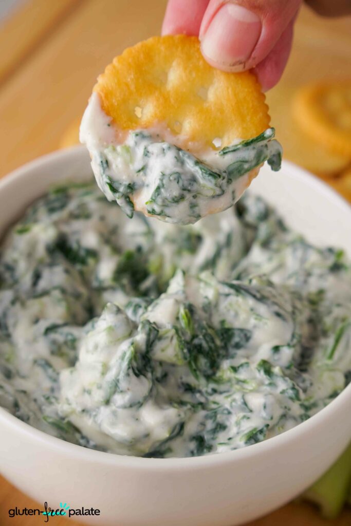 Spinach dip in a white bowl with a cracker being dipped into it. Photo by Gluten-Free Palate.