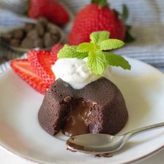 Gluten-Free Lave Cake with a chocolate center, topped with whipped cream and a spring of mint, on a white plate.