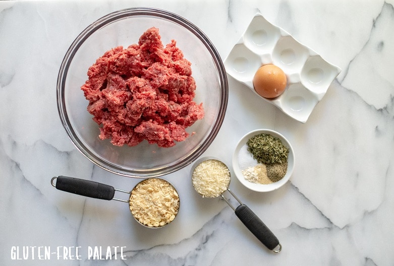 Ingredients to make gluten-free meatballs, ground beef, crushed crackers, cheese, spices and an egg