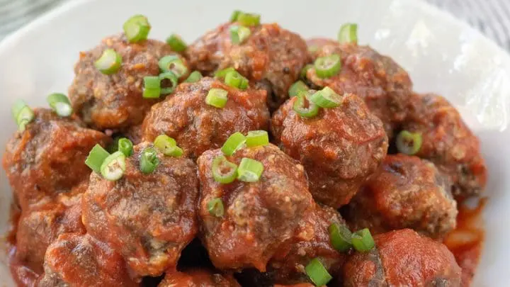 Gluten-Free Meatballs covered in marinara sauce and chopped green onions, on a white plate