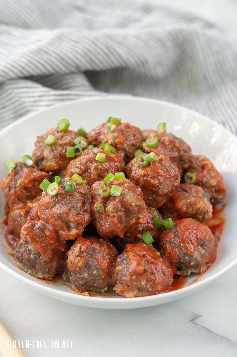 Gluten-Free Meatballs covered in marinara sauce and chopped green onions, on a white plate