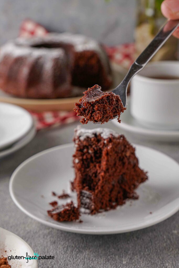 A slice of Gluten-free chocolate bundt cake on a white plate with a fork taking a bite.