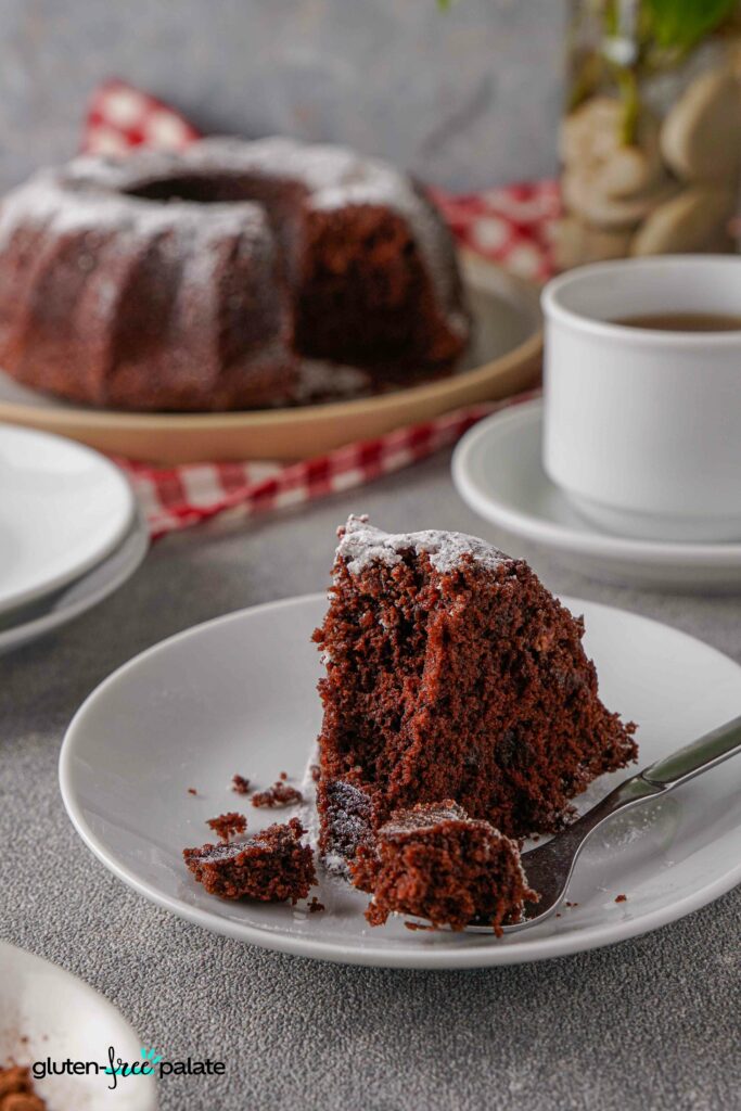 A slice of Gluten-free chocolate bundt cake on a white plate with a fork holding a piece.