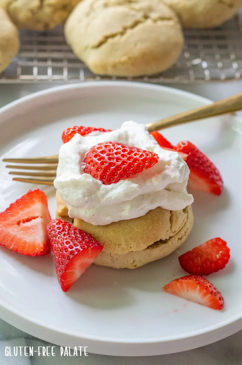 shortcake on a white plate topped with whipped cream and strawberries and a gold fork