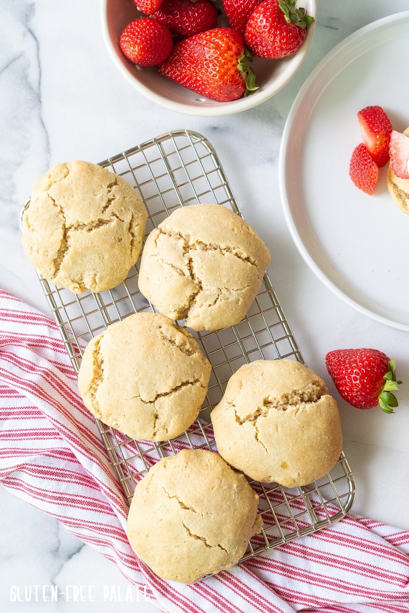shortcakes on a wire cooling rack over a white and red towel next to a bowl of strawberries