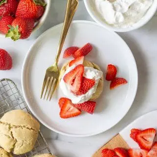 Paleo Strawberry Shortcake on a white plate with sliced strawberries with strawberries, whipped cream and shortcakes around it