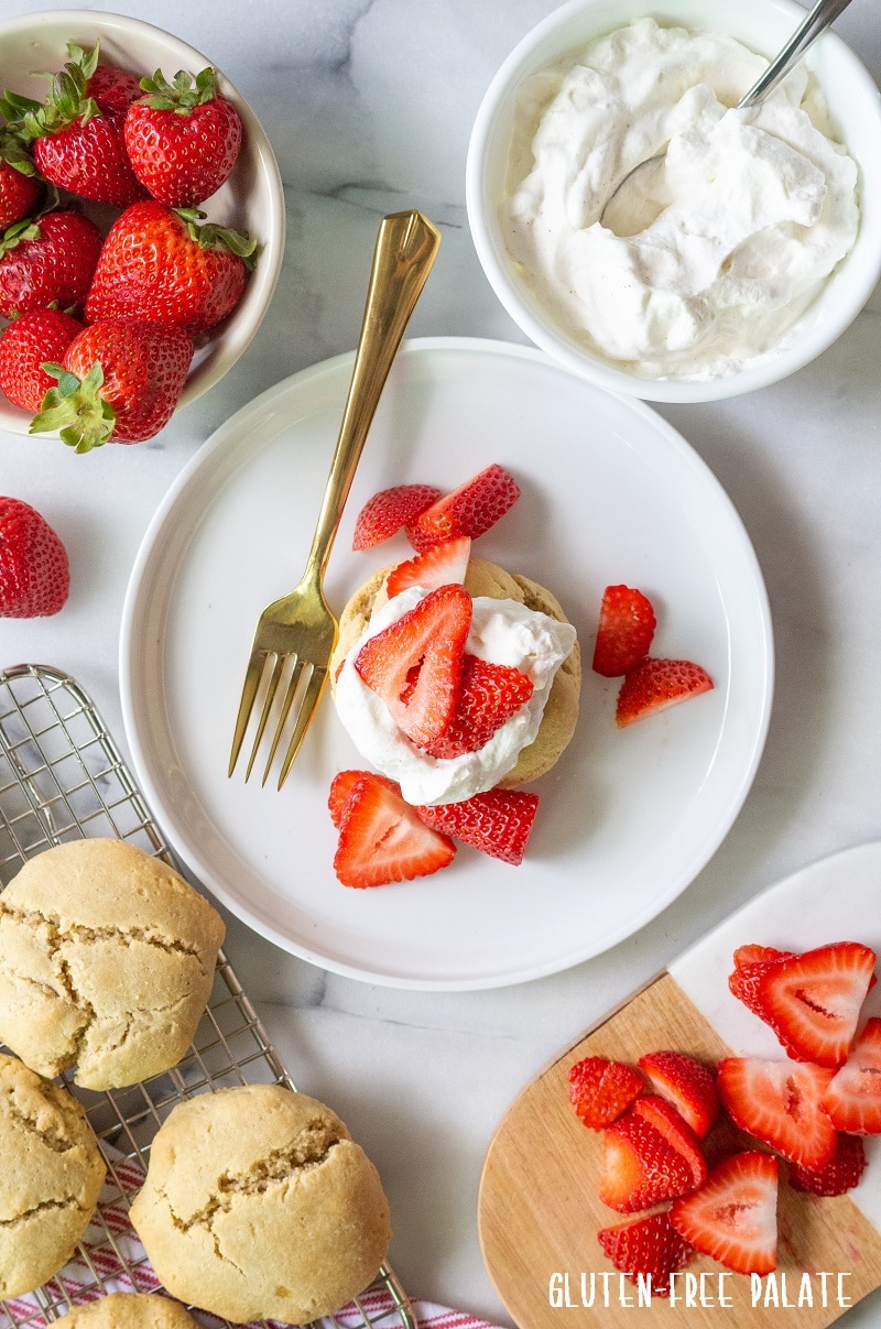 Paleo Strawberry Shortcake on a white plate with sliced strawberries with strawberries, whipped cream and shortcakes around it