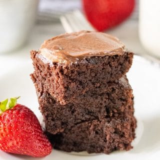 three gluten-free brownies stacked on a white plate with two strawberries