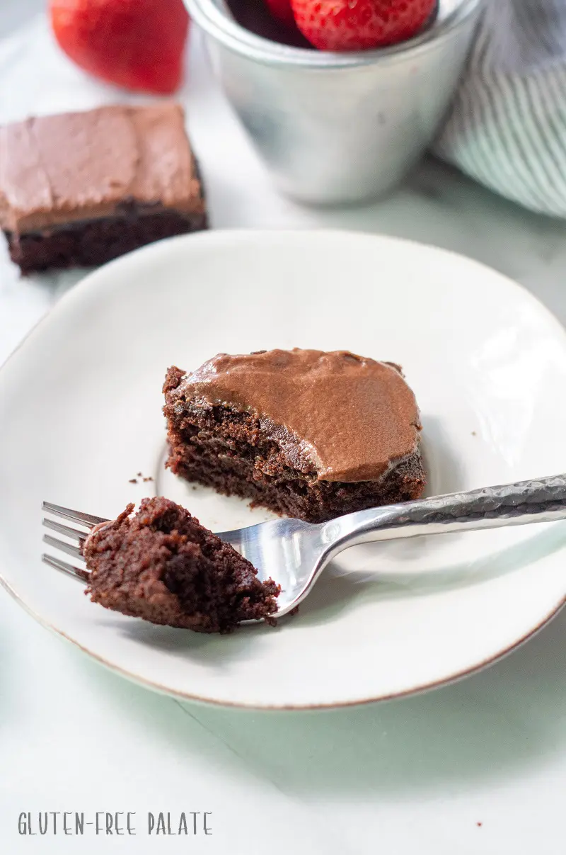 gluten-free brownies topped with chocolate frosting on a white plate with a fork taking a bite out