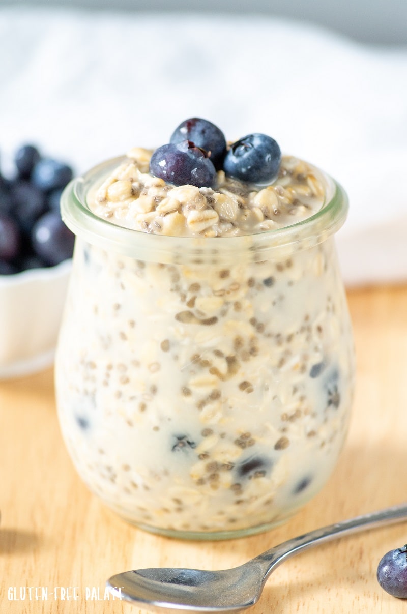 blueberry overnight oats in a glass jar with three blueberries on top and a spoon next to it