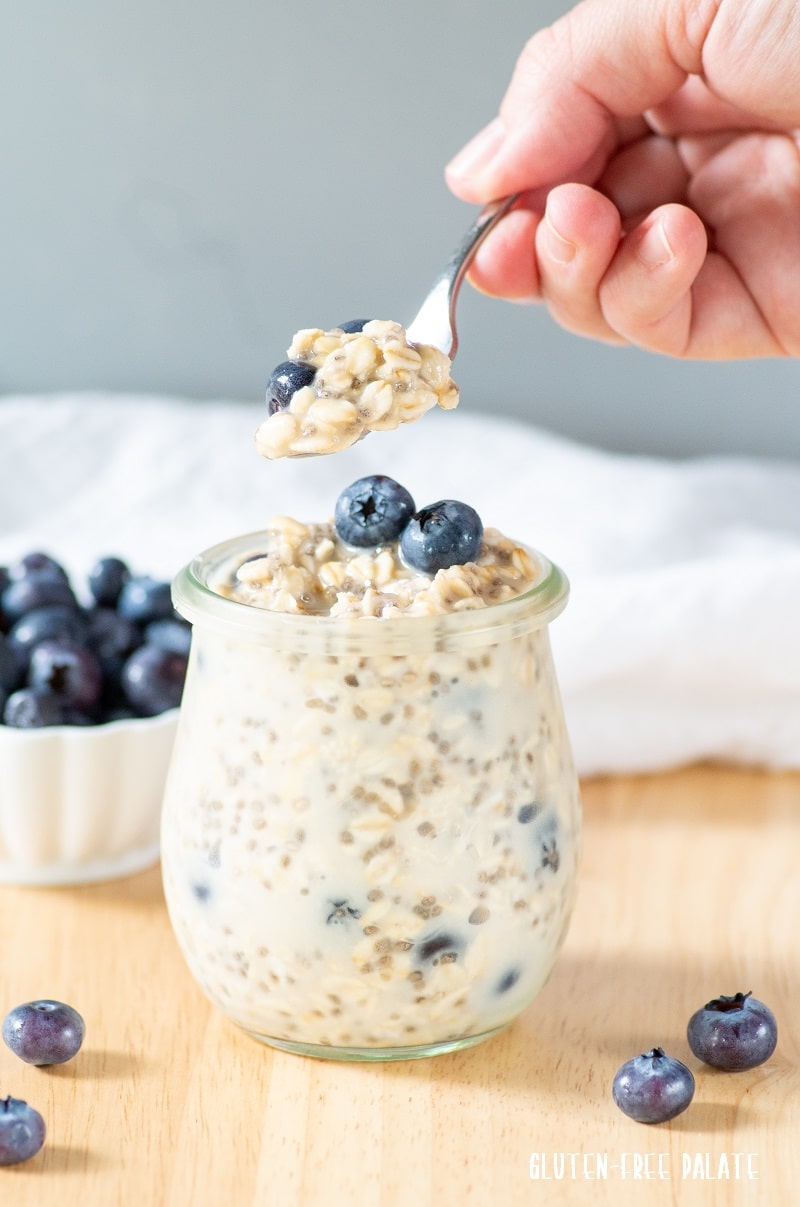 blueberry overnight oats in a jar with blueberries on top, a spoon with oats on it