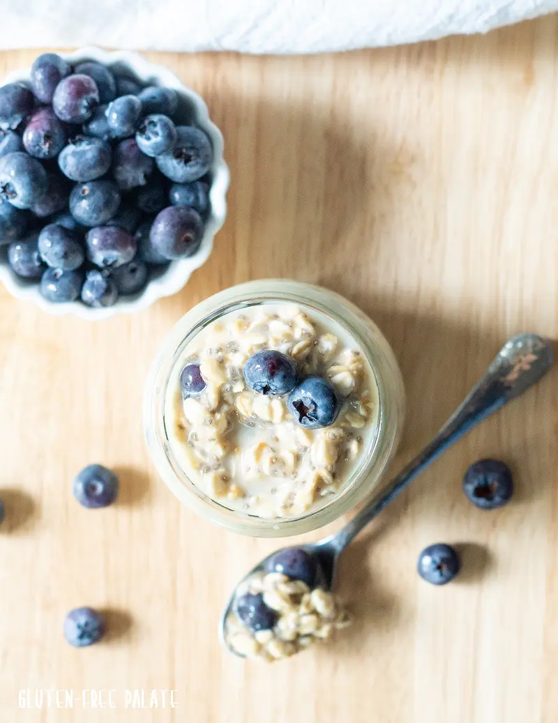 top down view of gluten-free overnight oats in a jar next to a spoon of overnight oats and a bowl of blueberries