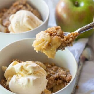Gluten-free apple crisp in a white bowl with ice cream, a spoon is taking a bite out