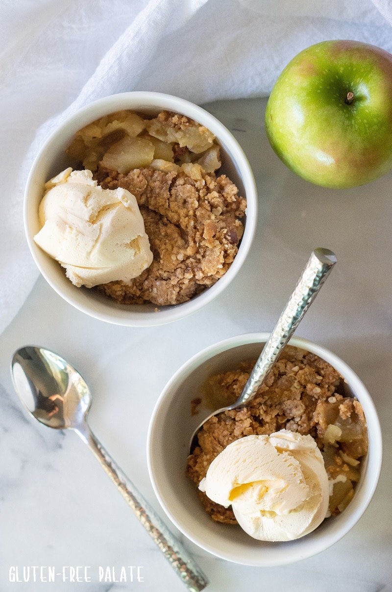 two white bowls filled with apple crisp with vanilla ice cream on top, with two poons