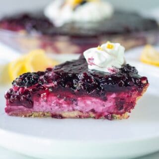 cream cheese pie with blackberries on a white plate, topped with whipped cream
