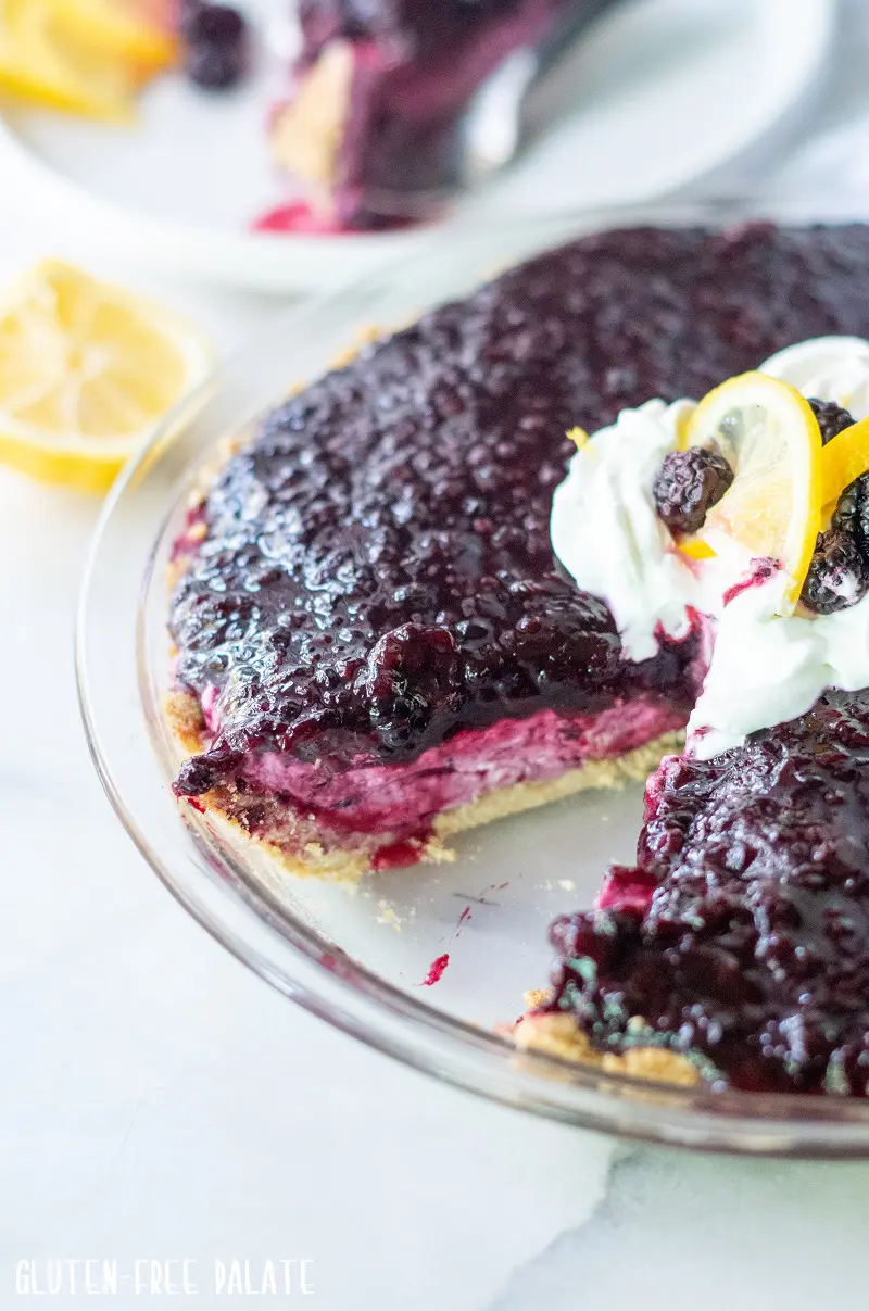 cream cheese pie with blackberries in a clear pie pan with a slice missing