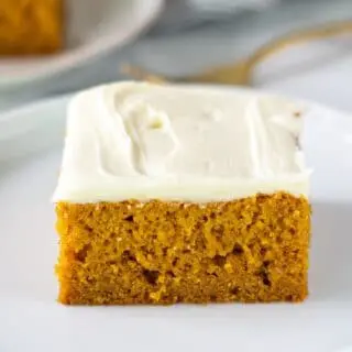 a square slice of gluten free pumpkin cake with white frosting on a white plate