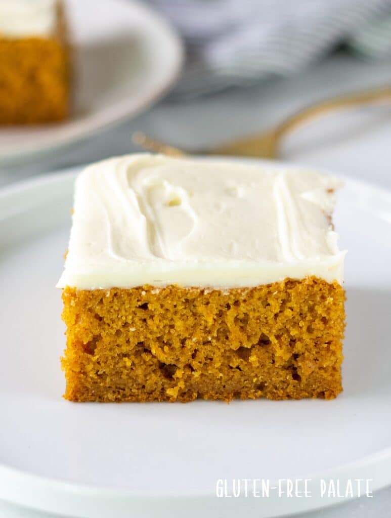 a square slice of gluten-free pumpkin cake with white frosting on a white plate