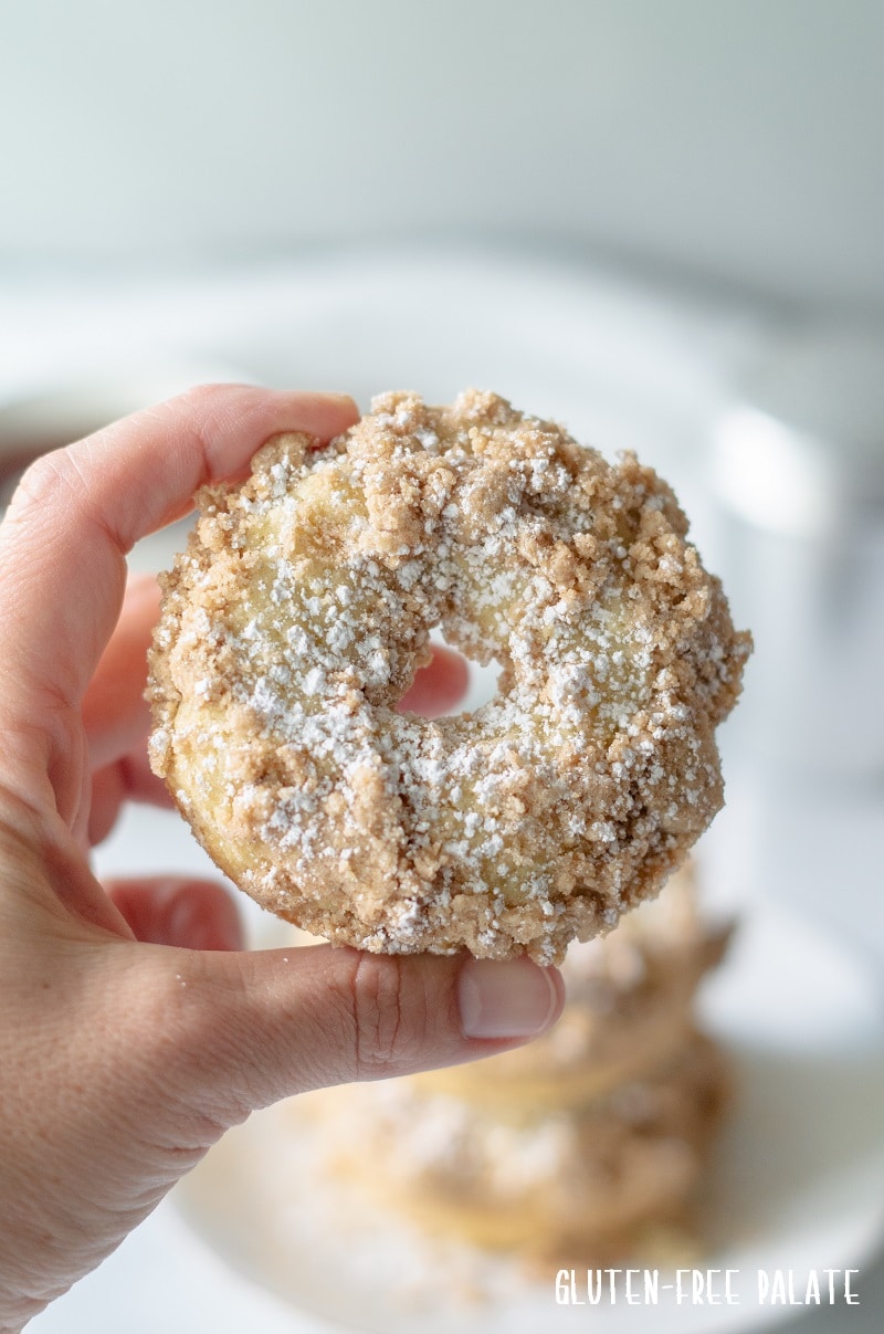 hand holding a round Gluten Free Crumb Cake Donut sprinkled with powdered sugar