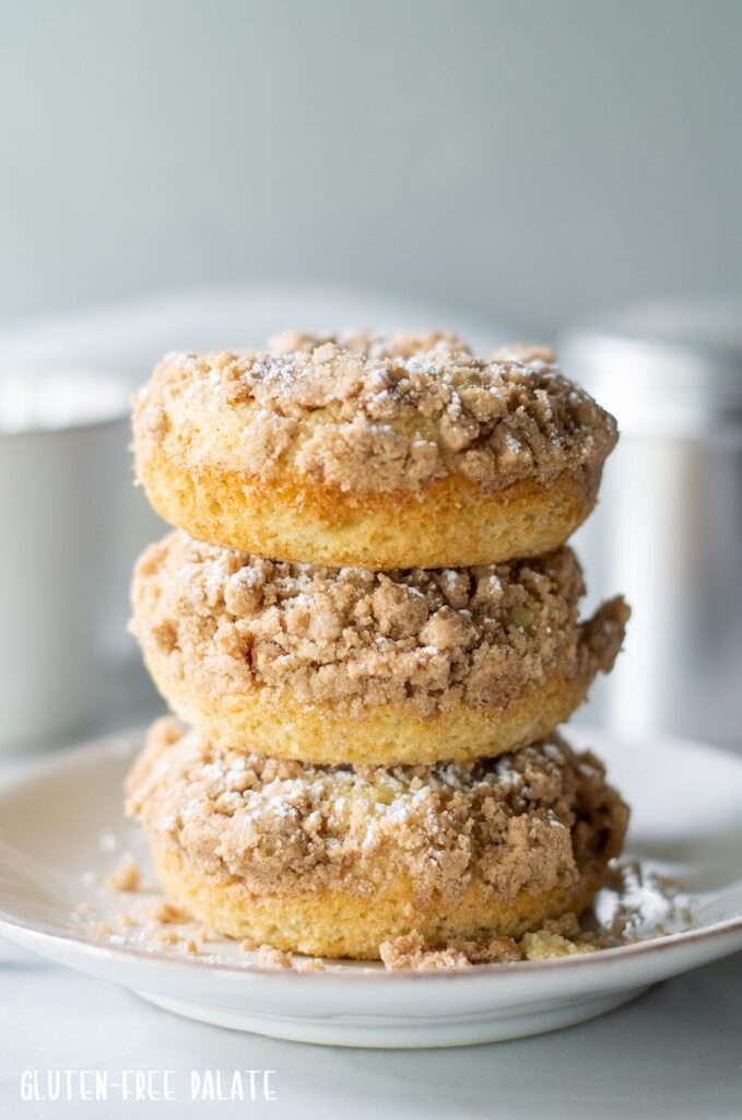Three gluten free crumb donuts stacked on a plate.