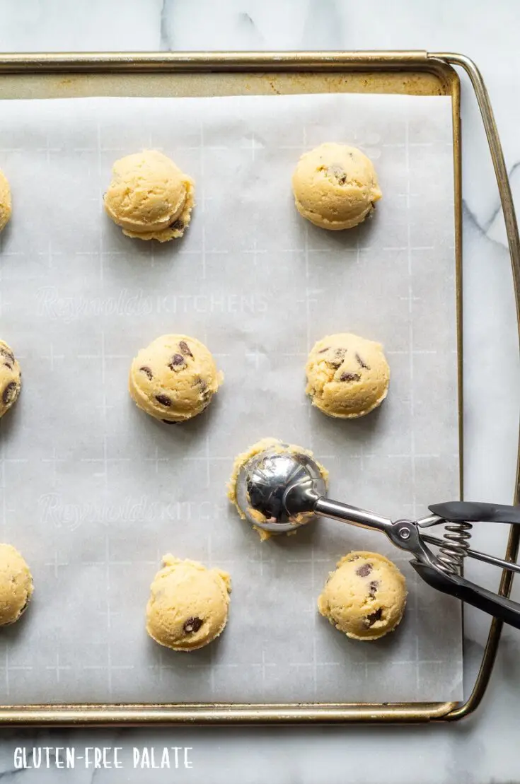 gluten-free chocolate chip cookie dough on a sheet pan with a cookie scoop