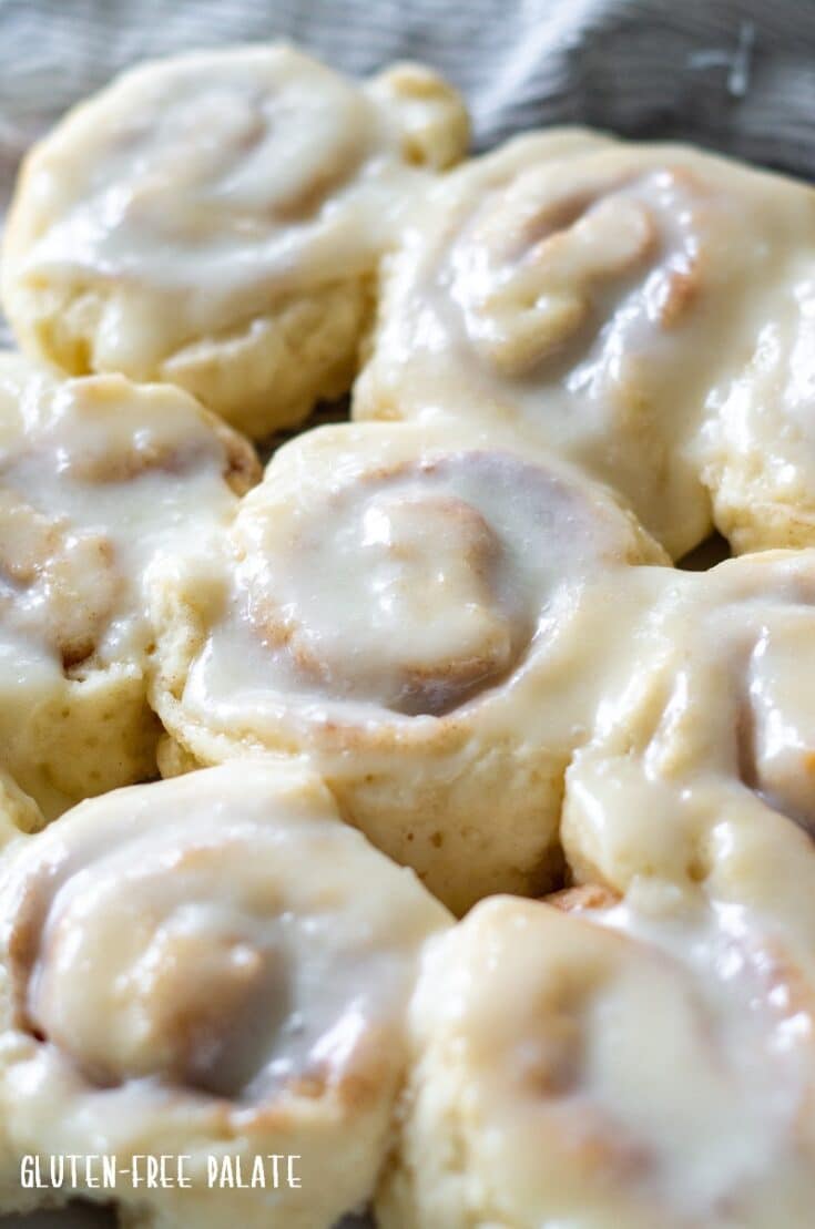 close up photo of round gluten free cinnamon rolls with white icing in a glass pan