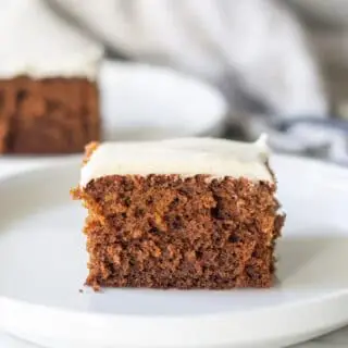 a slice of borwn Gluten-Free Gingerbread Cake with white frosting on a white plate