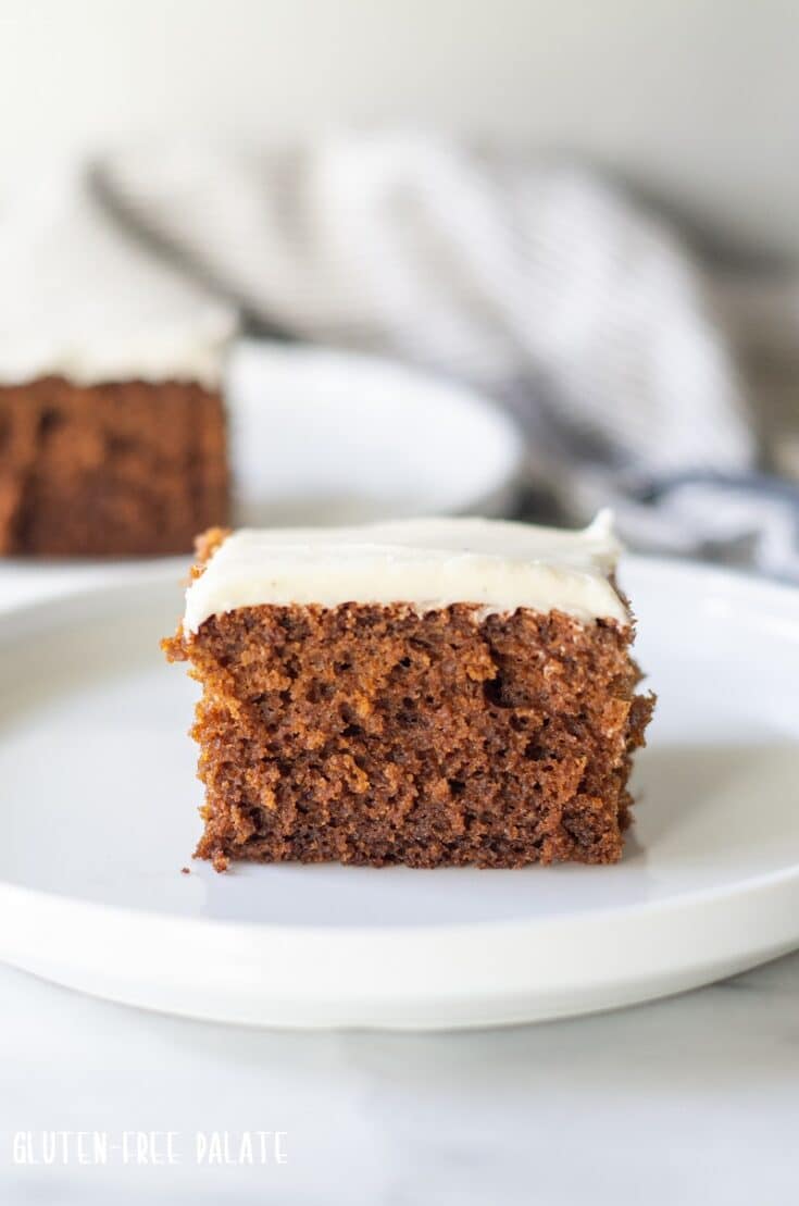 a slice of borwn Gluten Free Gingerbread Cake with white frosting on a white plate
